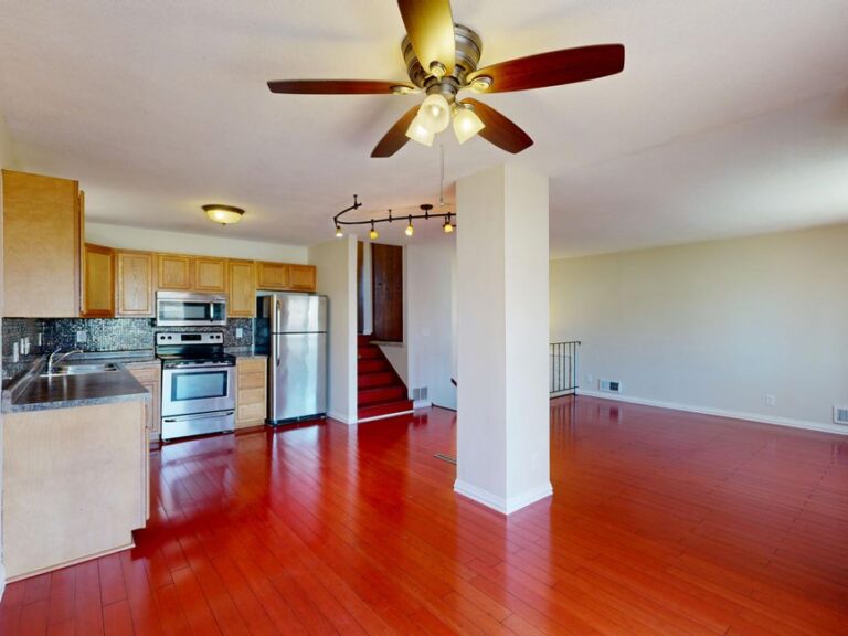 A person taking bright, clear photos of a tidy living room and kitchen in a clean, sunlit home